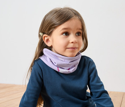 Mädchen mit braunen Haaren und Haarspange trägt ein blaues Langarmshirt und ein lila Halstuch mit Einhornmuster.