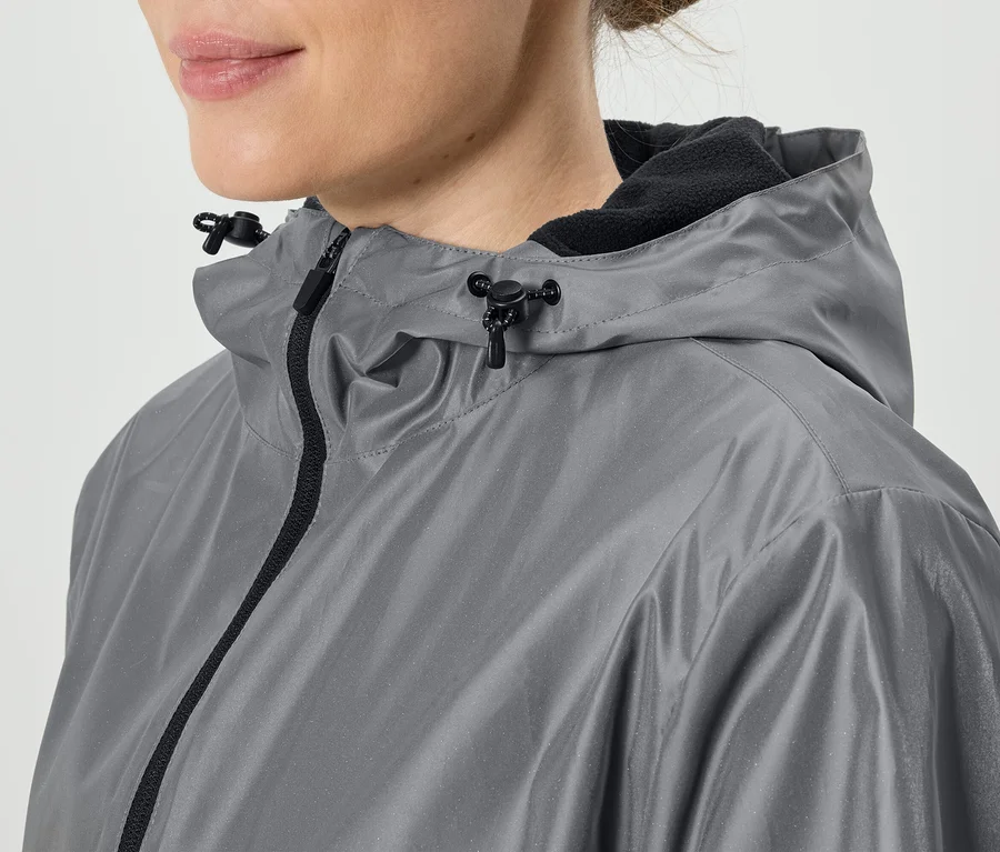Nahaufnahme einer Frau, die eine graue Regenjacke mit Kapuze und schwarzem Reißverschluss trägt.