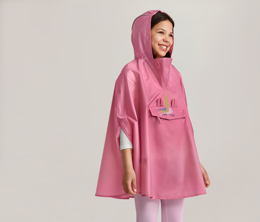Lächelndes Mädchen mit Kapuze trägt einen rosa Poncho mit Einhorn-Motiv und einer Tasche auf der Vorderseite.