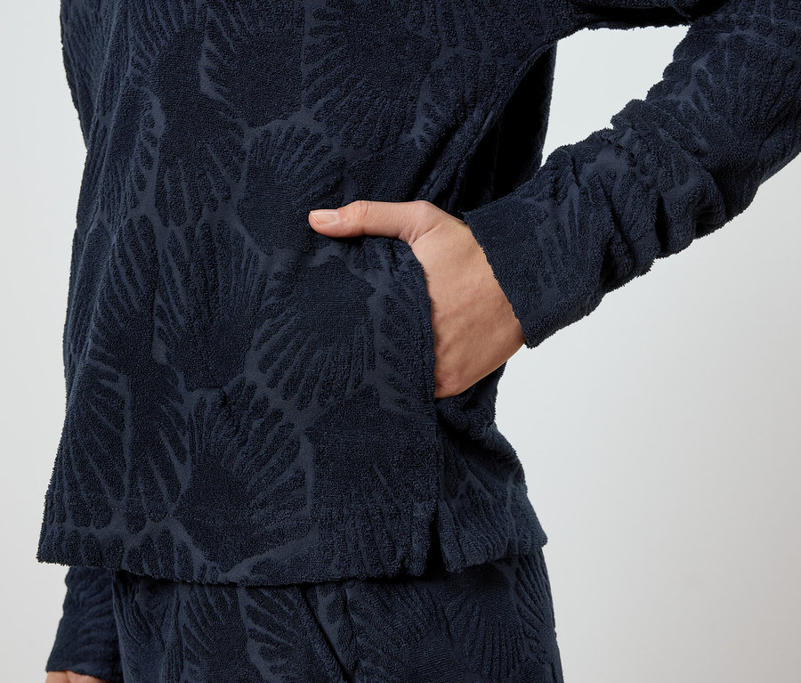 Person steckt Hand in die Tasche eines marineblauen Pullovers mit Blattmuster.