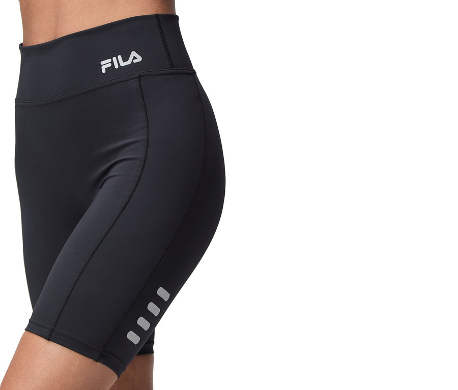 Nahaufnahme einer Person, die schwarze Fila-Radlerhosen trägt, mit dem Fila-Logo am Bund und reflektierenden Details an den Beinen.