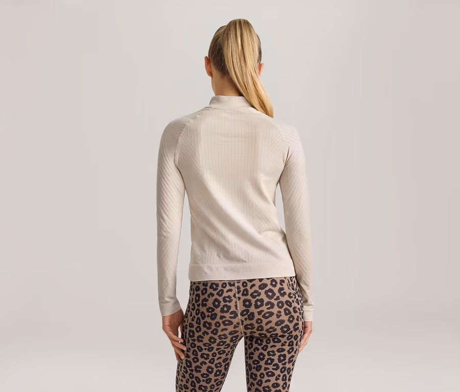 Frau von hinten, trägt ein hellbeiges, geripptes Langarmshirt mit Stehkragen und Leggings mit Leopardenmuster.