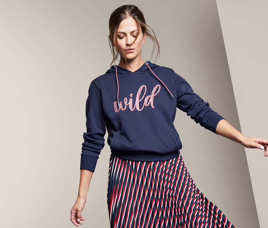 Frau posiert in Plisseerock und Kapuzensweatshirt mit Text-Print.
