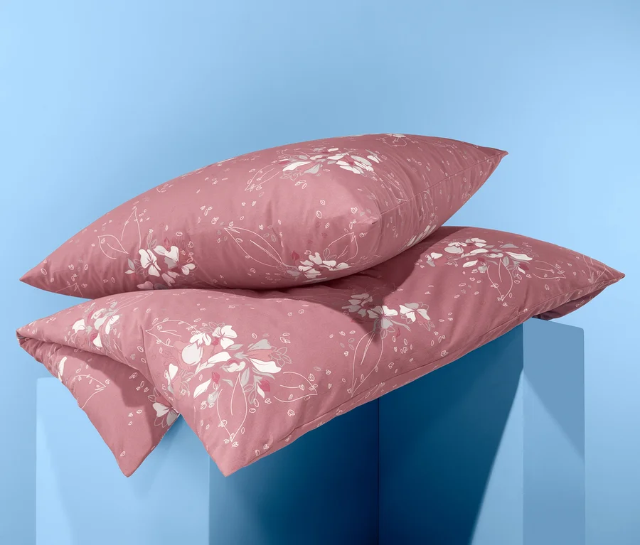 Zwei Jersey-Bettwäsche Normalgröße mit Blumenmuster liegen gestapelt auf einem blauen Sockel.