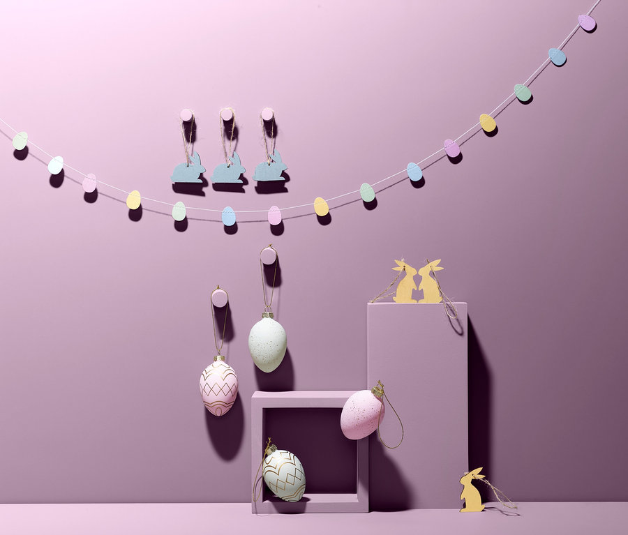 Ein Deko-Geschenkset mit Anhängern in Form von Eiern und Hasen hängt an einer lila Wand.
