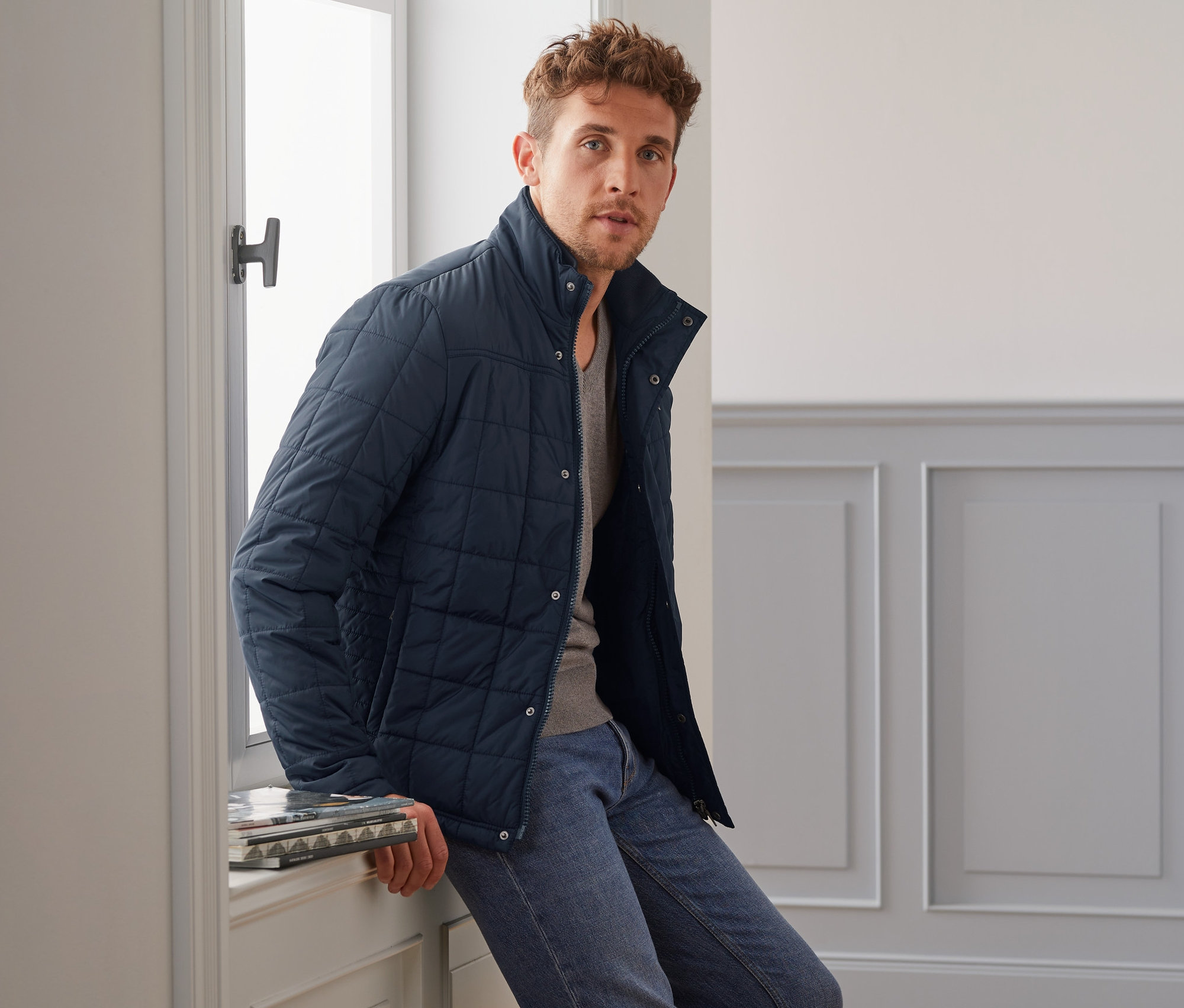 Mann sitzt auf Fensterbank und trägt eine blaue Steppjacke.