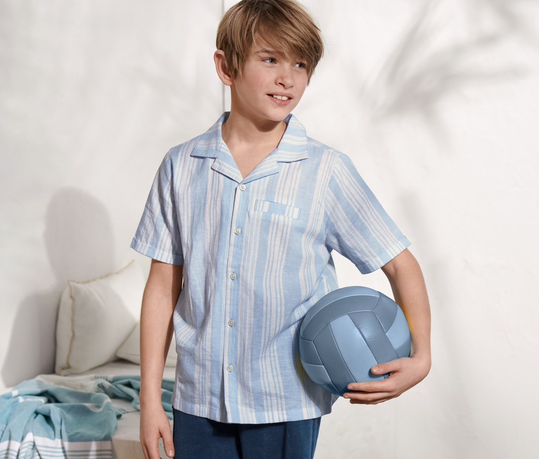 Junge hält blauen Volleyball und trägt ein Kurzarmhemd aus Bio-Baumwolle.