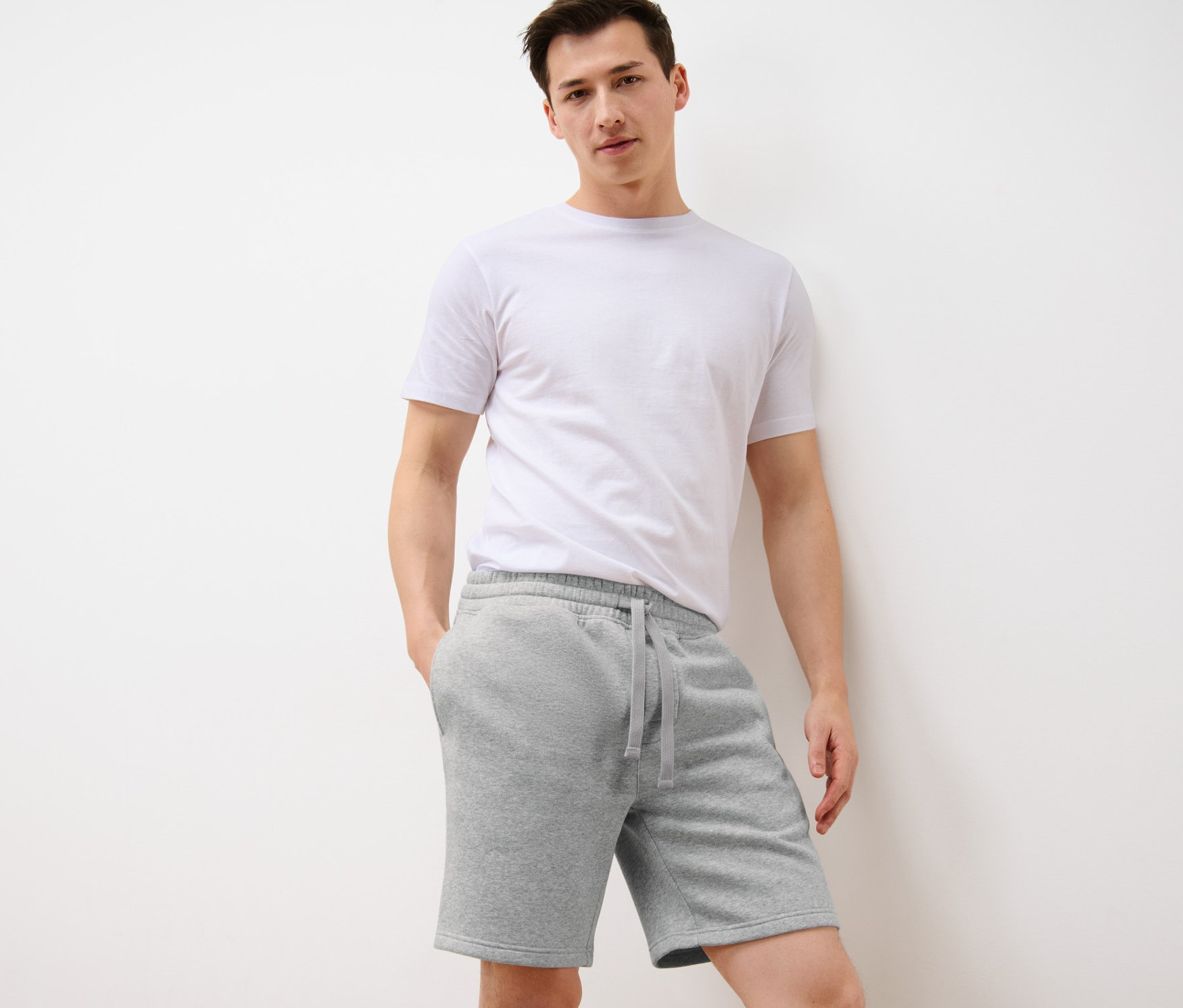 Mann steht mit Händen in den Taschen der hellgrauen Sweatshorts.