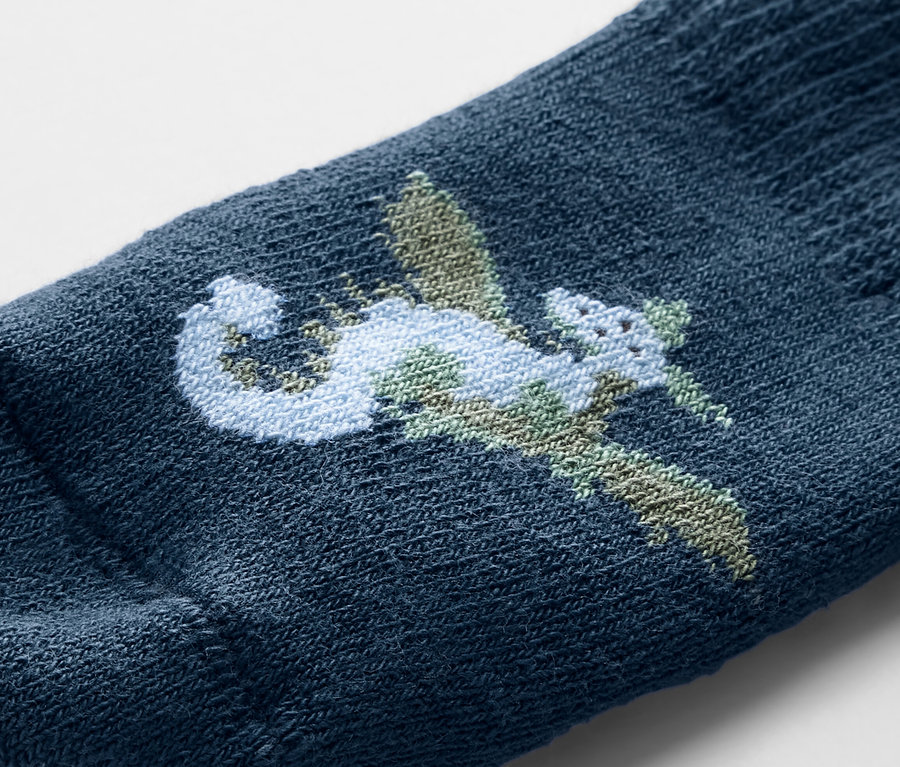 Detailaufnahme einer blauen Babysocke mit Drachen-Stickerei.