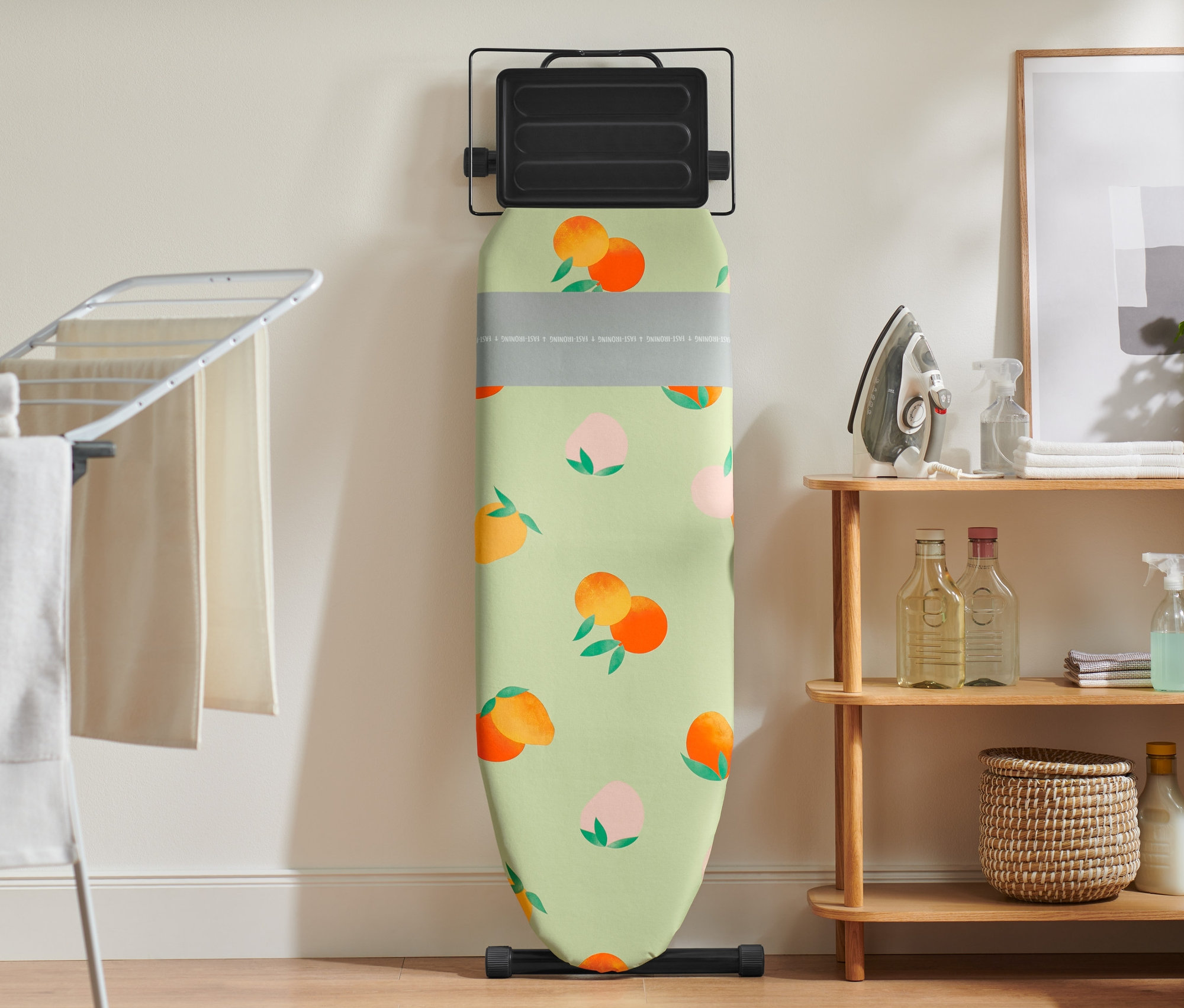 Ein Bügelbrett mit einem Bügelbrettbezug mit Pfirsichmuster lehnt an einer Wand.