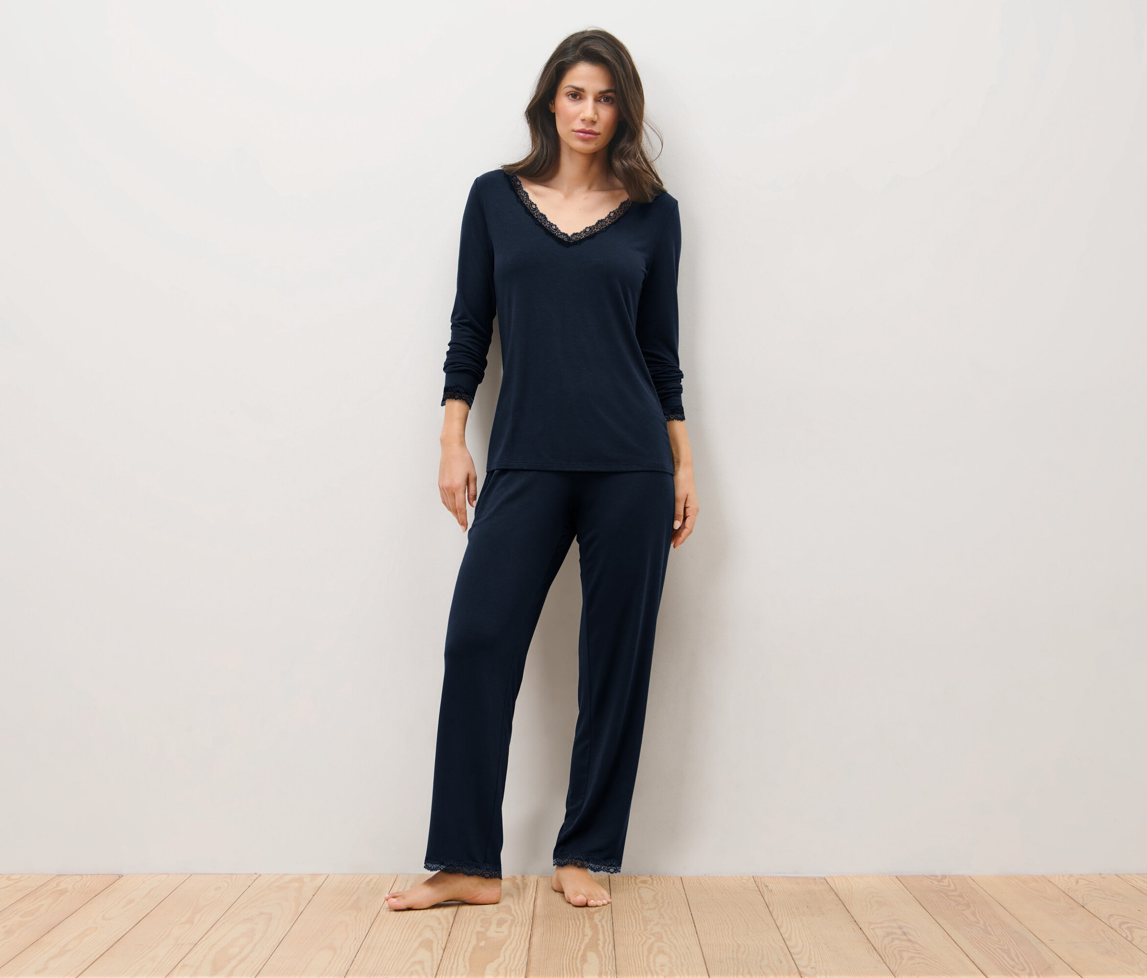 Frau steht auf einem Holzboden und trägt einen dunkelblauen Pyjama.