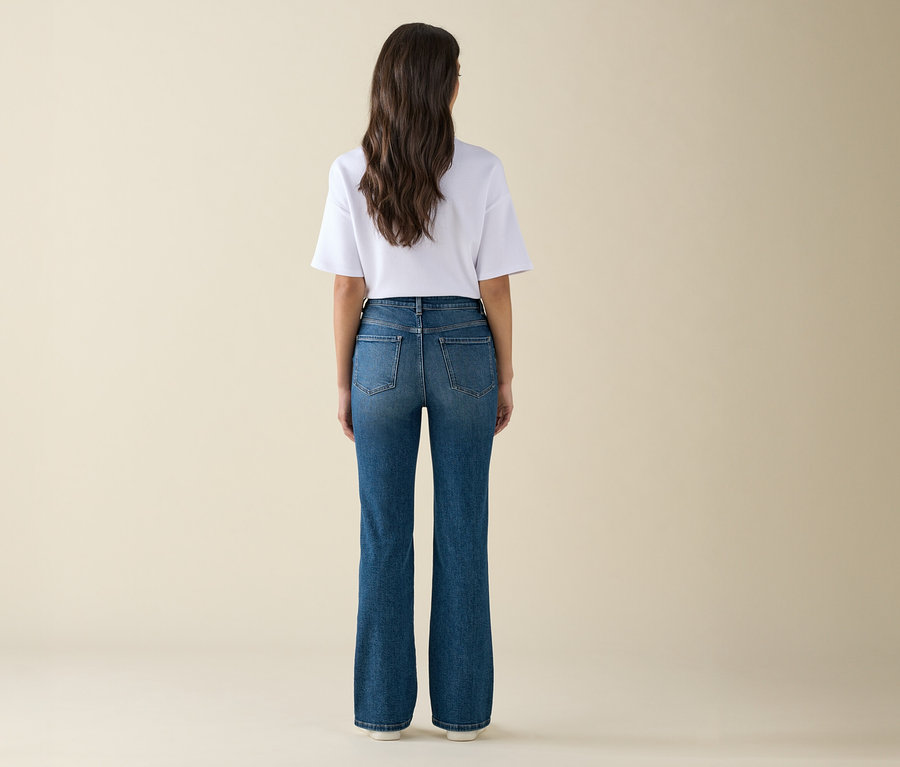 Eine Frau mit langen braunen Haaren steht mit dem Rücken zur Kamera und trägt ein weißes T-Shirt und blaue Jeans.