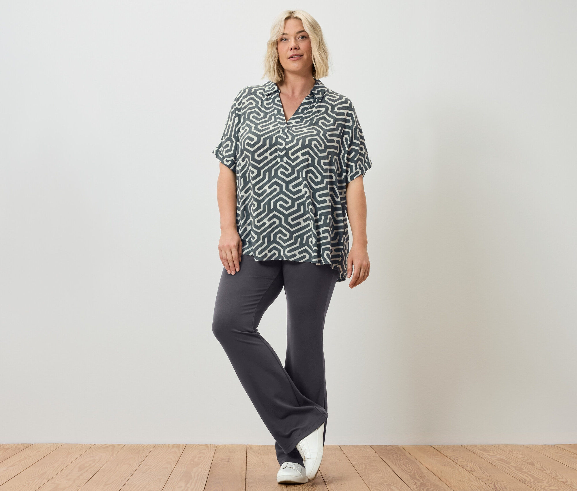 Eine Frau posiert in ausgestellten Leggings und einer bedruckten Bluse.