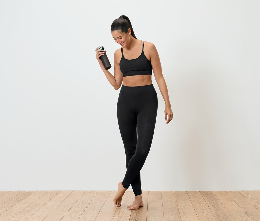 Frau in schwarzer Sportbekleidung hält eine Trinkflasche.