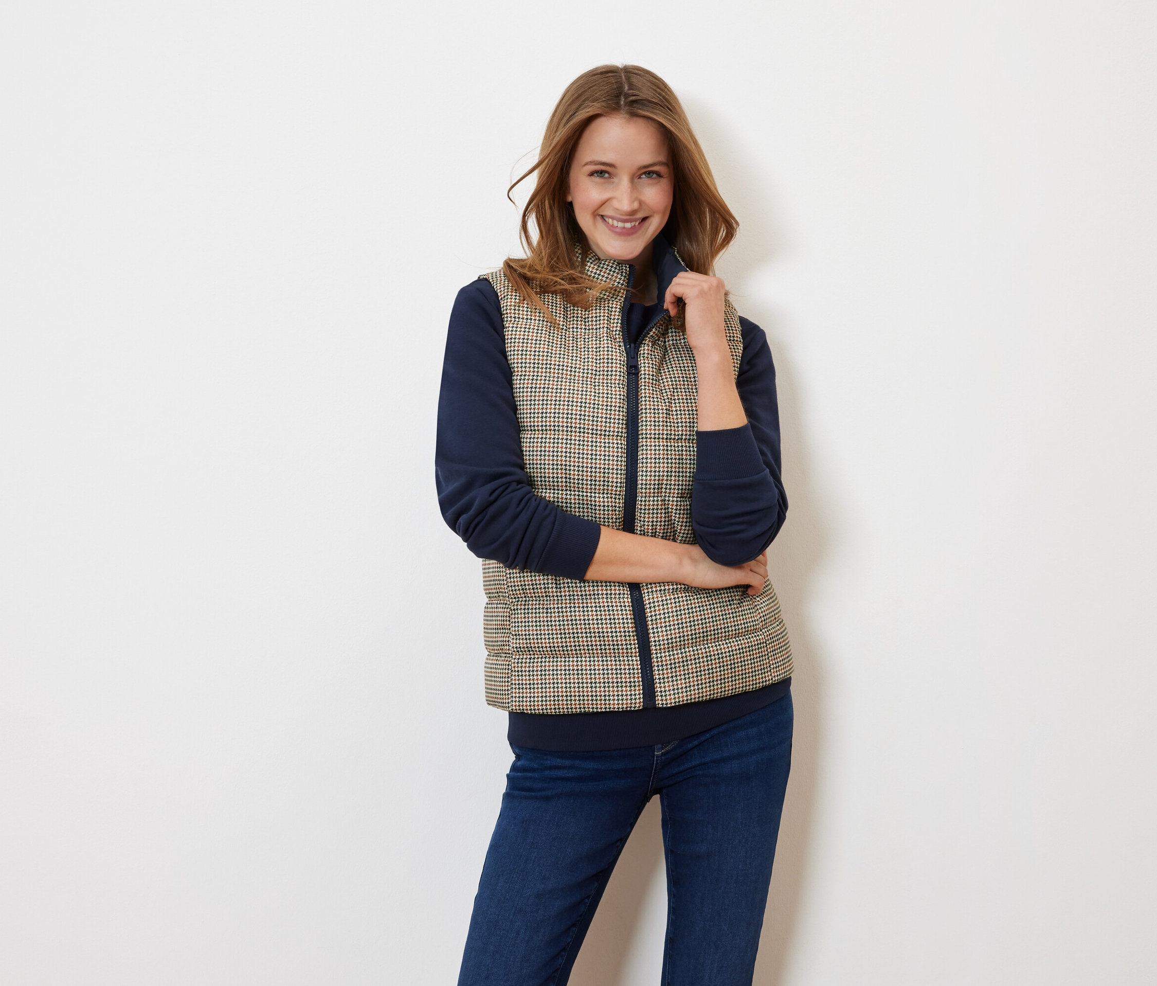 Frau posiert mit gesteppter Weste und marineblauem Oberteil.