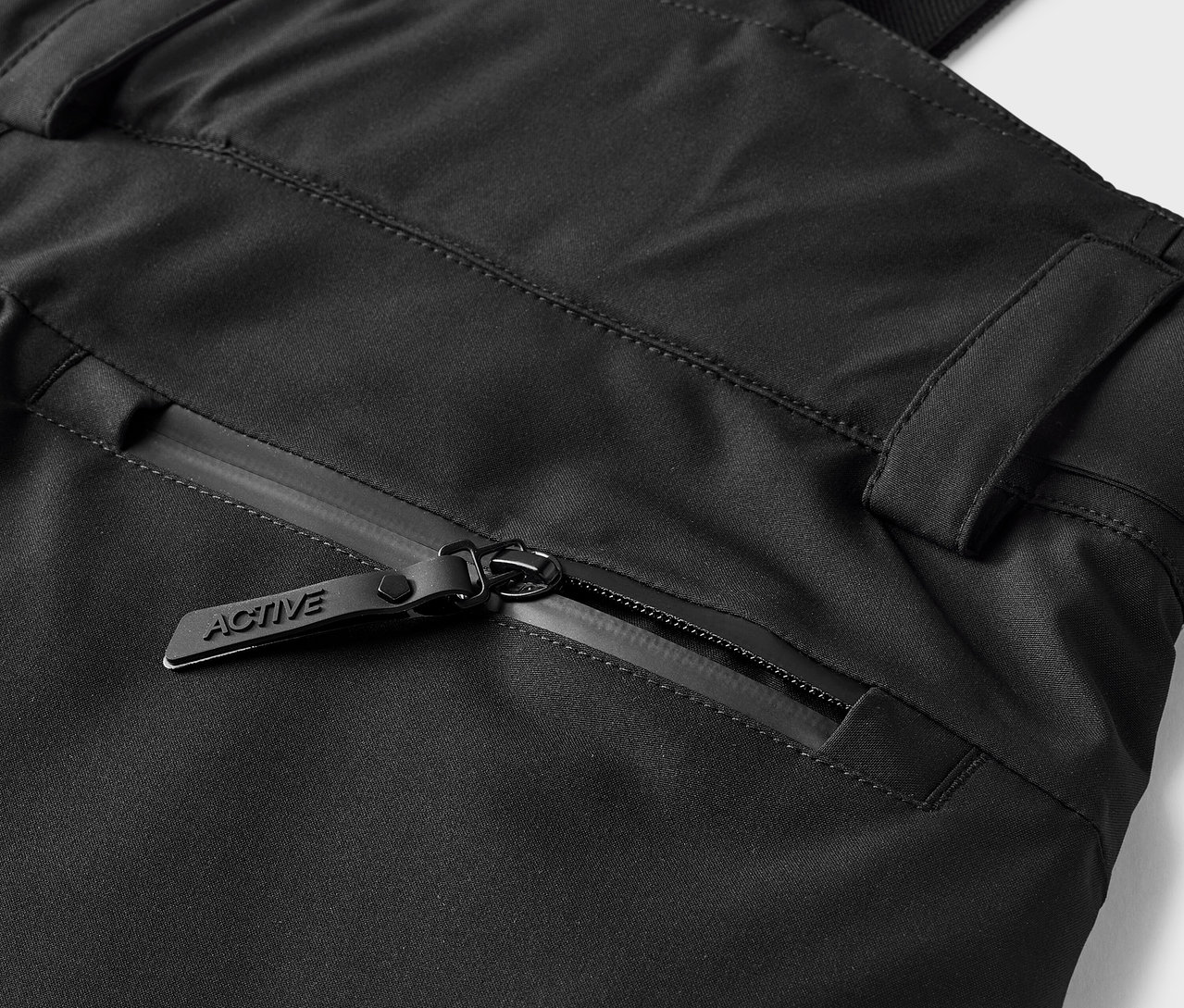 Detail einer schwarzen Hose mit einer Reißverschlusstasche und einem Schieber mit der Aufschrift ACTIVE.