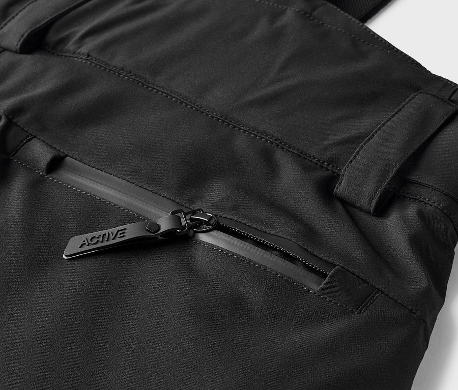 Detail einer schwarzen Hose mit einer Reißverschlusstasche und einem Schieber mit der Aufschrift ACTIVE.