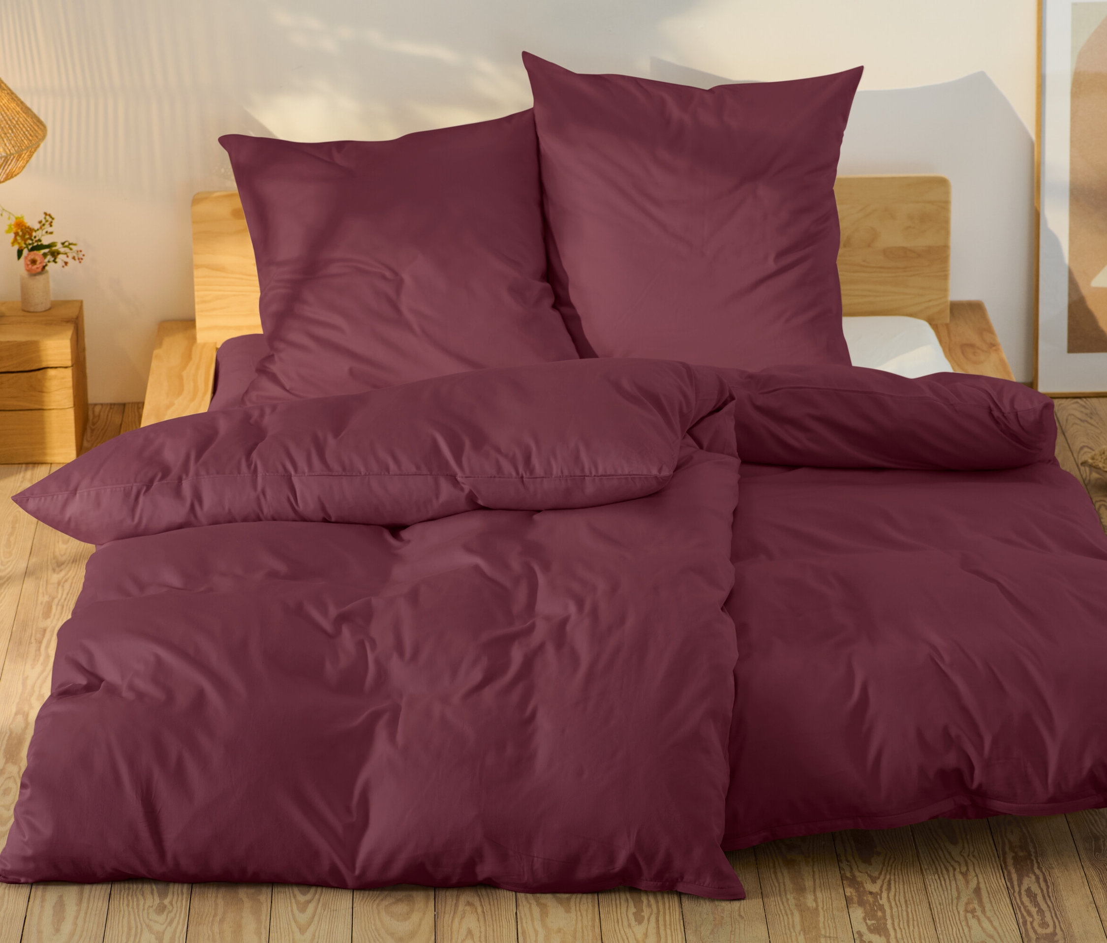 Burgunderfarbene Bettwäsche auf einem Bett mit Holzrahmen.