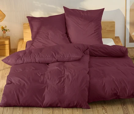 Burgunderfarbene Bettwäsche auf einem Bett mit Holzrahmen.