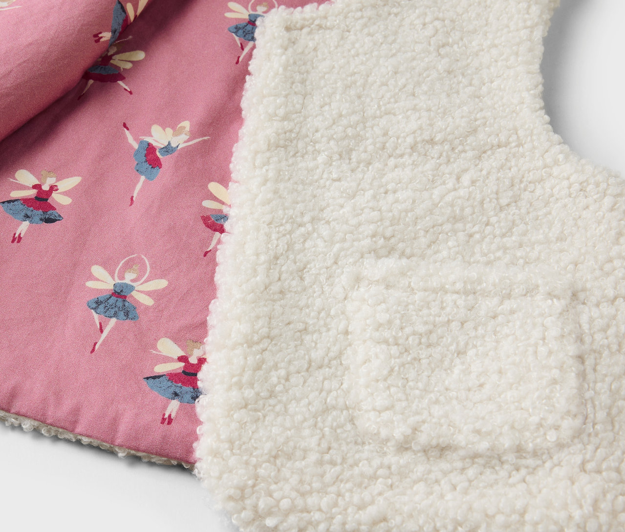 Detail einer Kinderweste mit rosa Futter mit Ballerina-Print und einer weißen Sherpa-Außenseite.