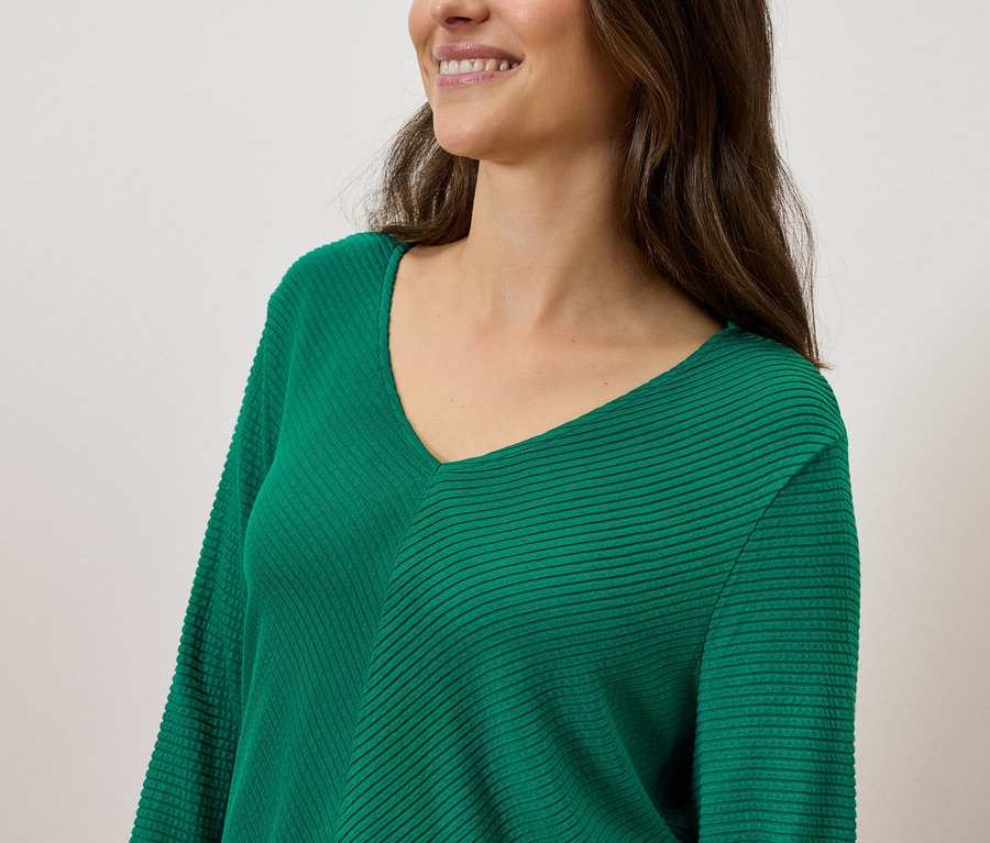 Lächelnde Frau mit braunem Haar, die einen grünen Pullover mit V-Ausschnitt trägt.