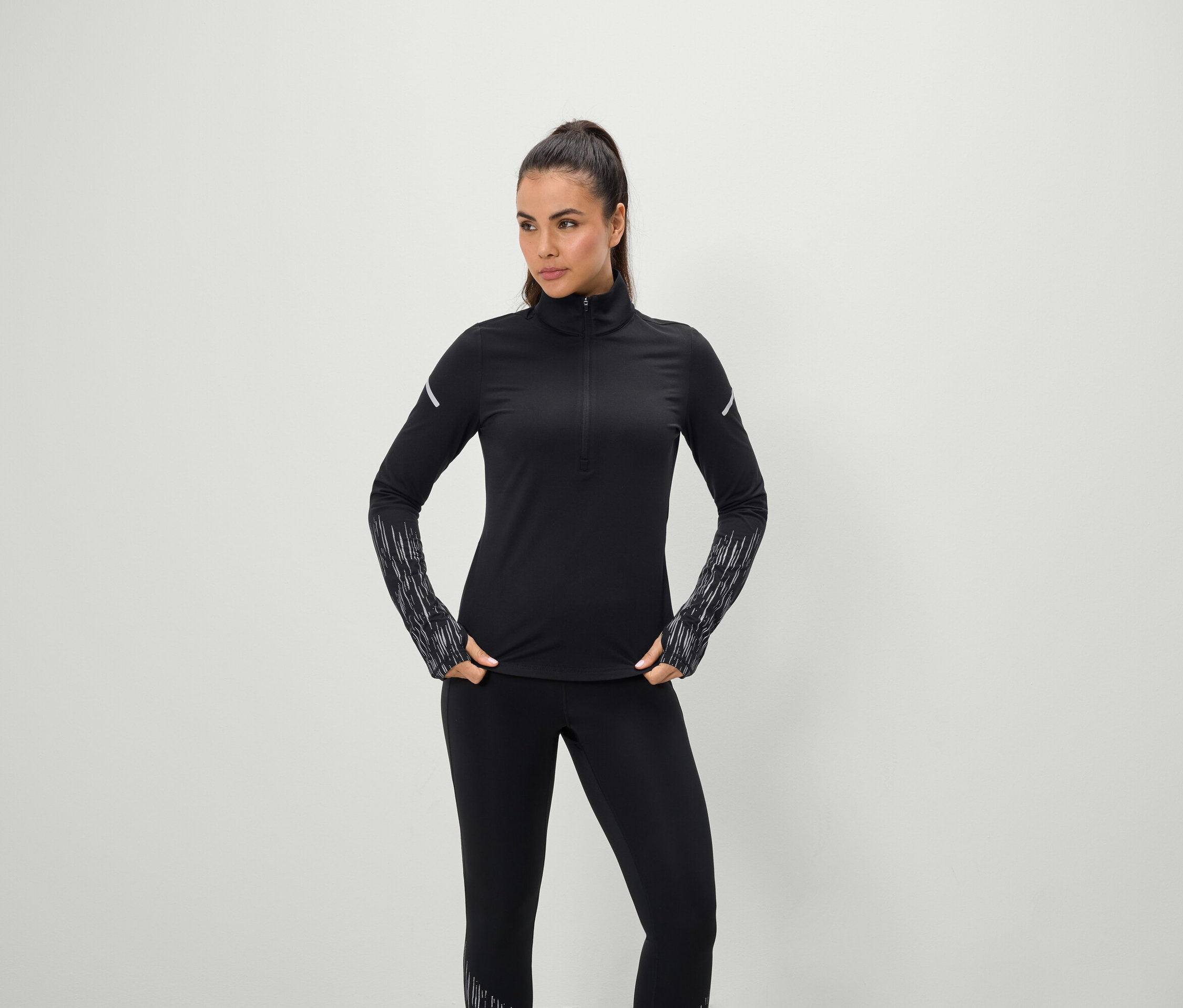 Frau posiert in schwarzer Sportbekleidung mit langärmligem Oberteil und Leggings.