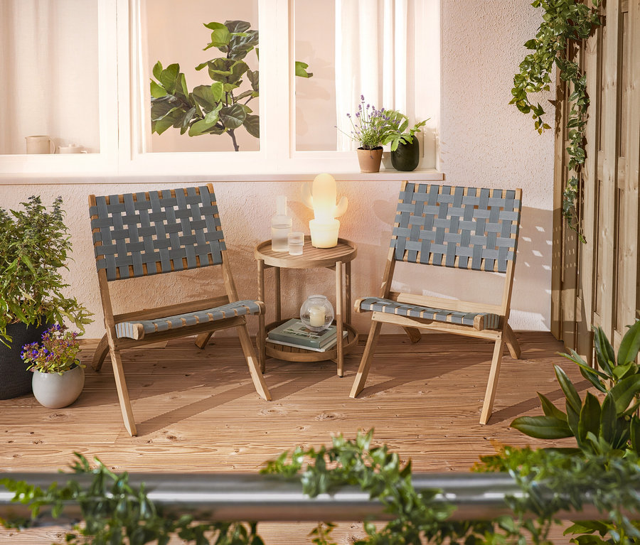 Zwei geflochtene Stühle und ein Beistelltisch stehen auf einer Terrasse.