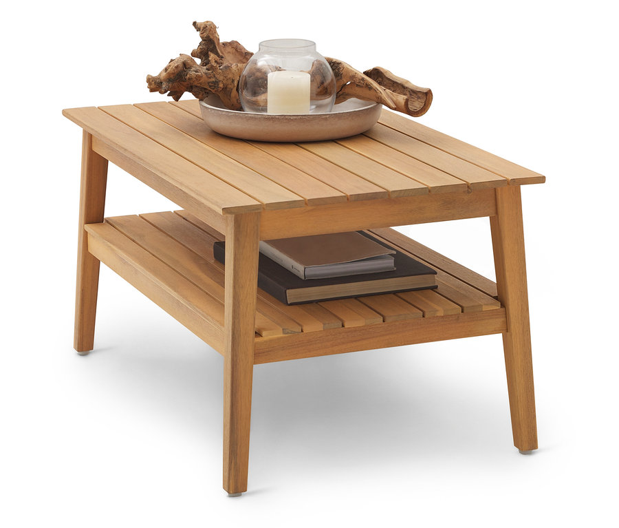 Ein hellbrauner Couchtisch aus Holz mit zwei Ebenen. Auf der oberen Ebene stehen eine Schale mit einer Kerze und Treibholz, auf der unteren Ebene liegen Bücher.