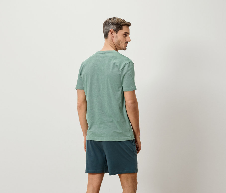 Mann von hinten, trägt ein grünes T-Shirt und blaue Shorts.