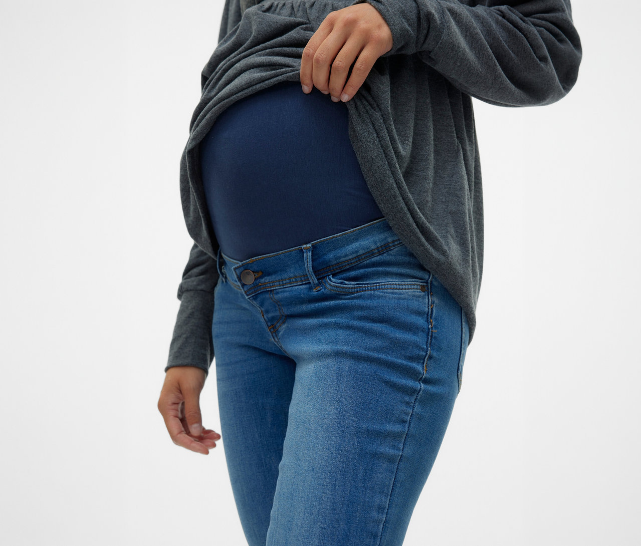 Frau hebt graues Oberteil über den Bauch, trägt MAMALICIOUS Skinnyjeans »MLMILA« und marineblaues Umstandsoberteil.