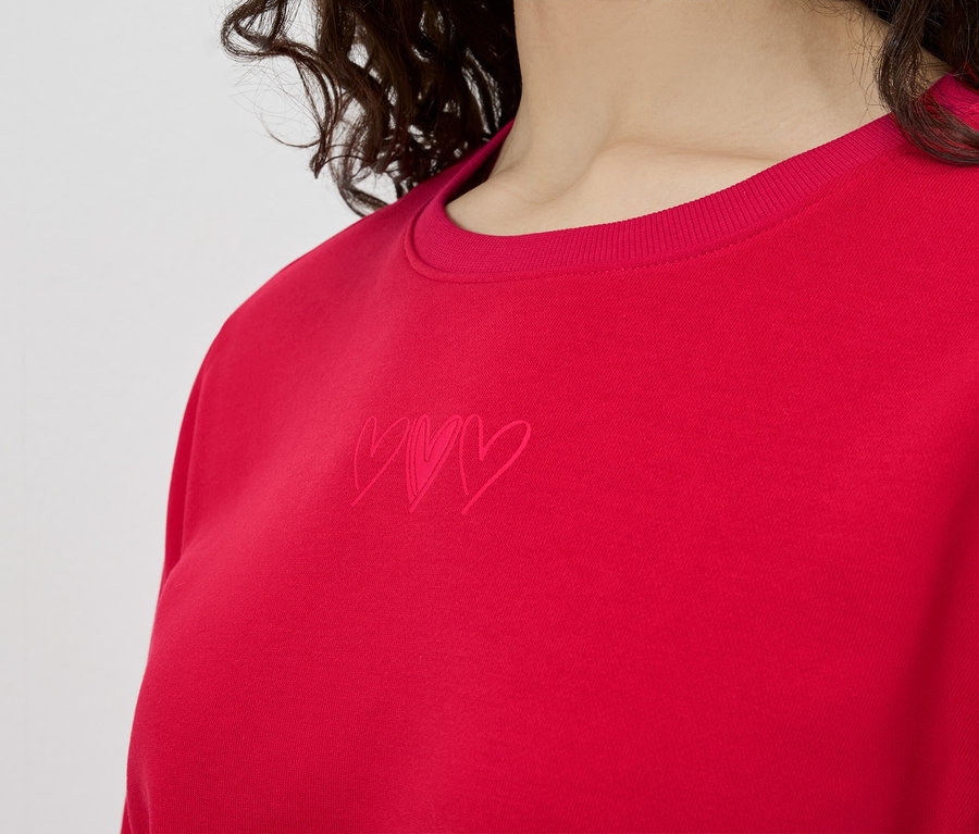 Nahaufnahme einer Frau, die ein rotes Sweatshirt mit drei kleinen Herzen trägt.