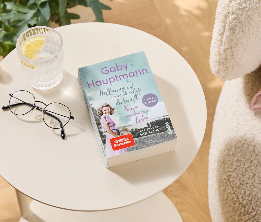 Auf einem Tisch liegen eine Brille, ein Glas Wasser mit Zitrone und das Buch "Hoffnung auf eine glückliche Zukunft" von Gaby Hauptmann.