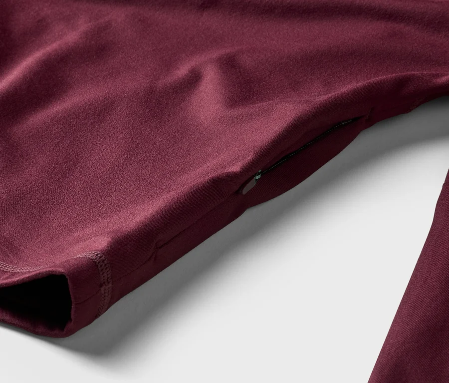 Nahaufnahme eines burgunderroten Langarmshirts mit Reißverschlusstasche am Ärmel, liegend auf einem weißen Hintergrund.