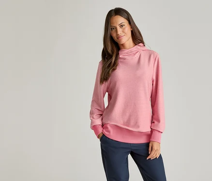 Frau mit braunen Haaren trägt einen gestreiften, rosa-weißen Pullover und blaue Hosen.