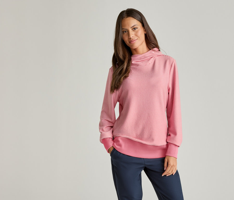 Frau mit braunen Haaren trägt einen gestreiften, rosa-weißen Pullover und blaue Hosen.