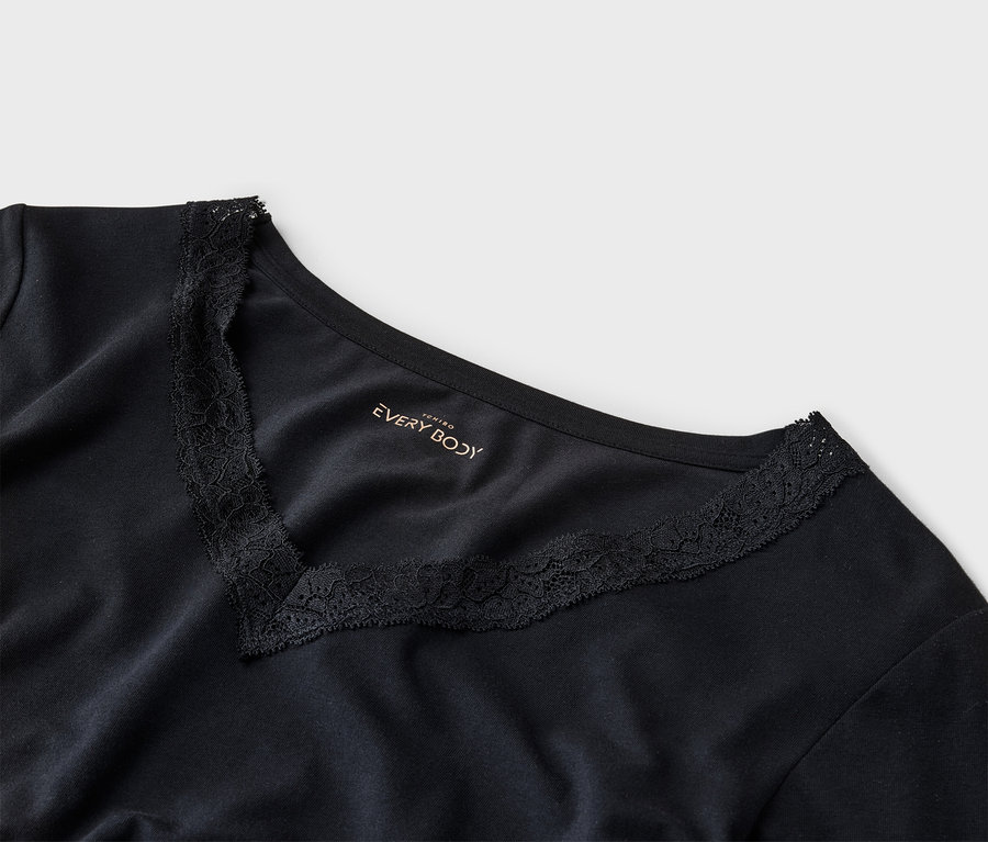 Nahaufnahme eines schwarzen T-Shirts mit V-Ausschnitt und Spitzenbesatz. Das "EVERY BODY"-Logo ist aufgedruckt.