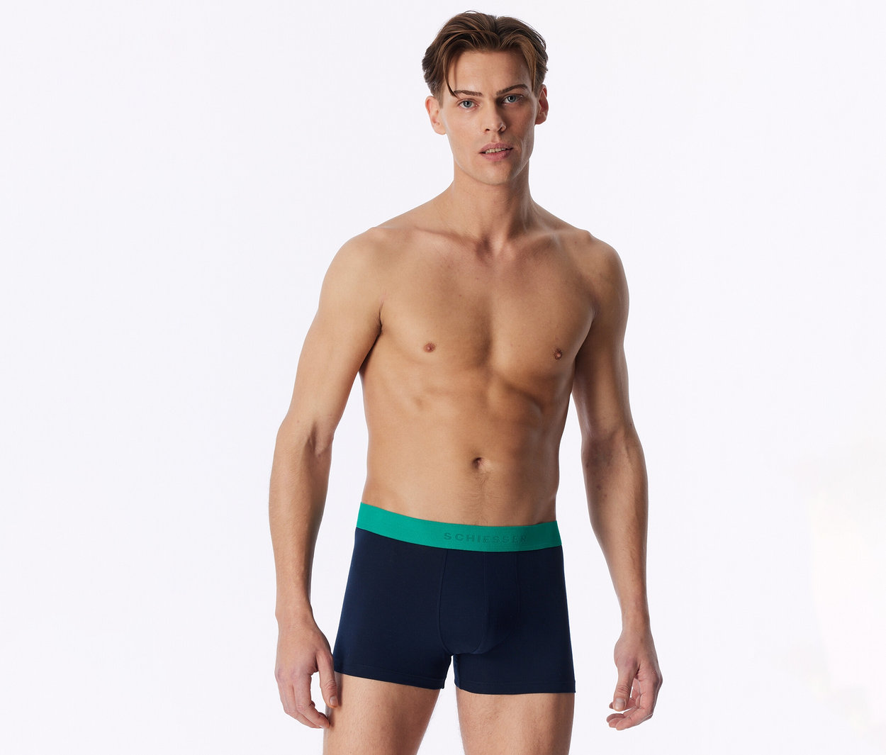 Ein oberkörperfreier Mann steht frontal und trägt marineblaue Boxershorts mit grünem Bund.