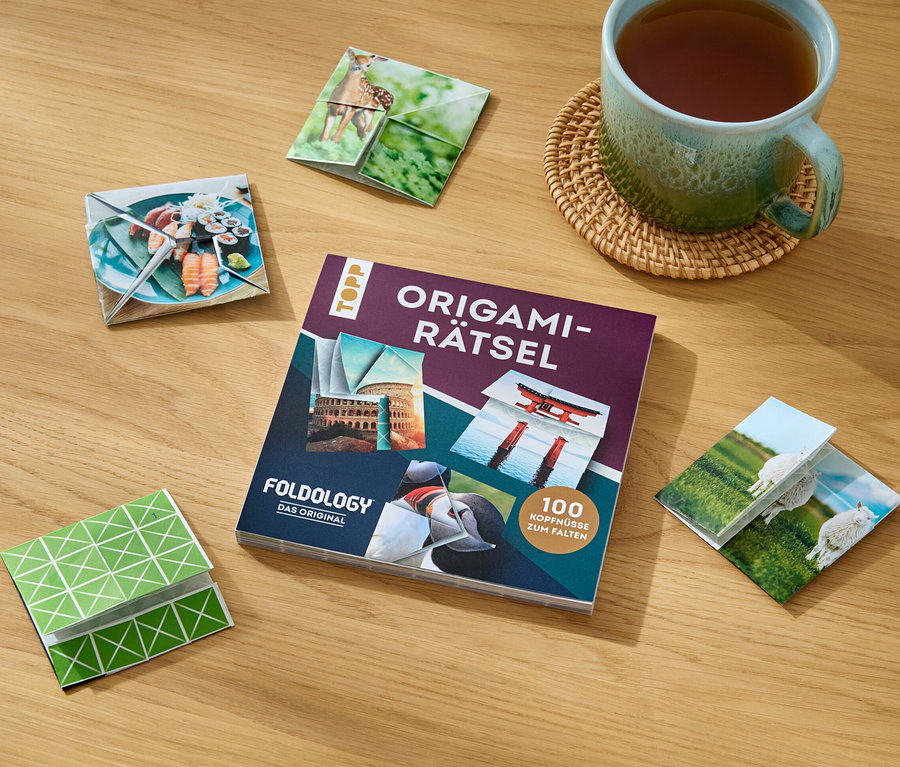 Auf einem Holztisch liegen das Buch »Origami-Rätsel«, eine Tasse Tee und gefaltete Origami-Figuren mit verschiedenen Motiven.