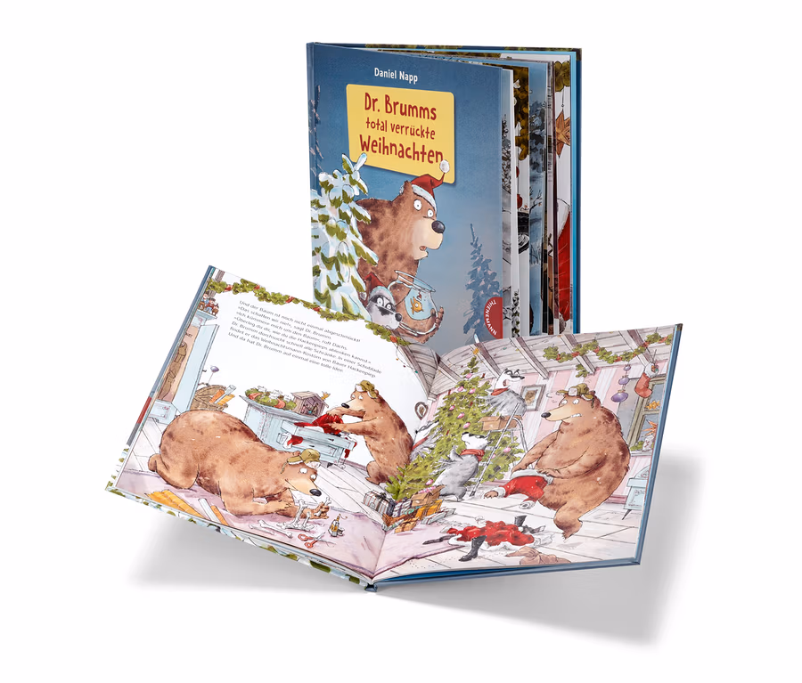 Offenes Buch "Dr. Brumms total verrückte Weihnachten" mit Illustrationen von Bären und Waschbären, die einen Weihnachtsbaum schmücken, im Hintergrund eine weitere Ausgabe des Buchs.