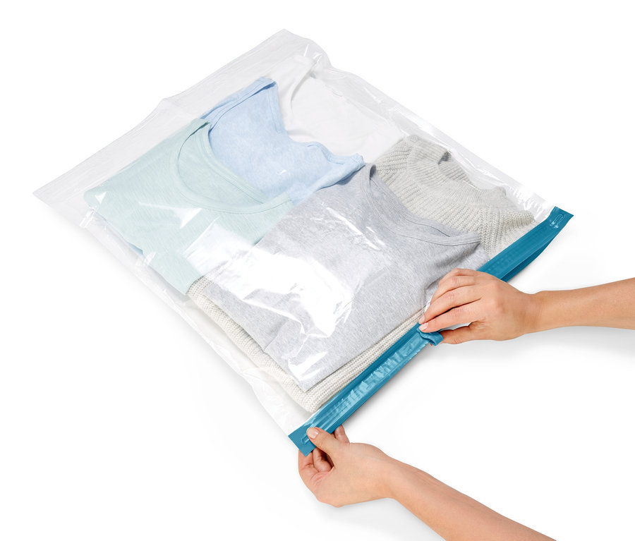 Hände verschließen einen Vakuum-Reisebeutel mit hellblauer, grauer und weißer Kleidung darin.