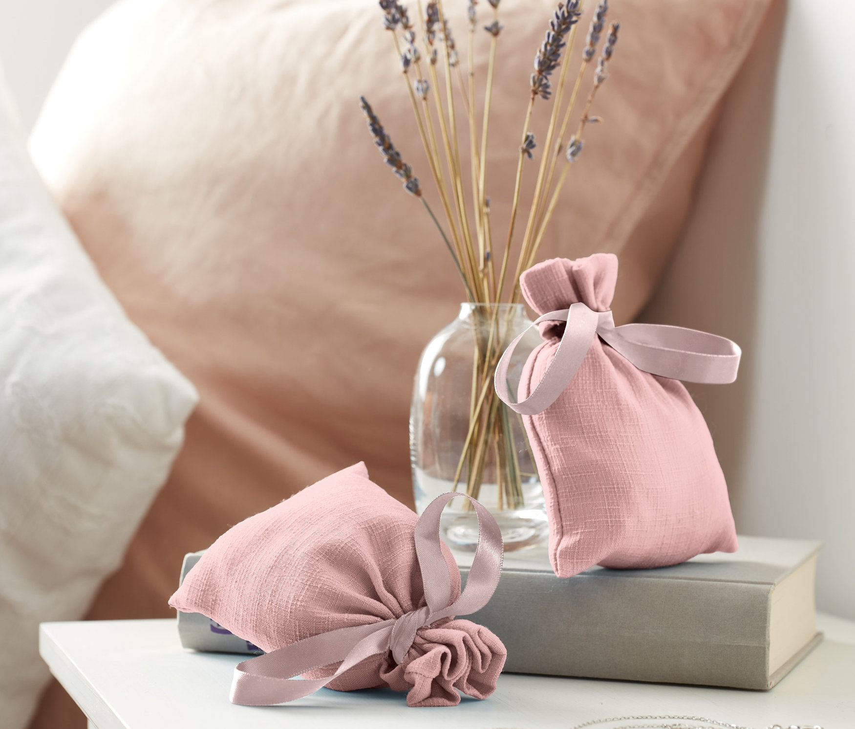 Zwei Duftsäckchen liegen auf einem Buch neben einer Vase mit Lavendel.
