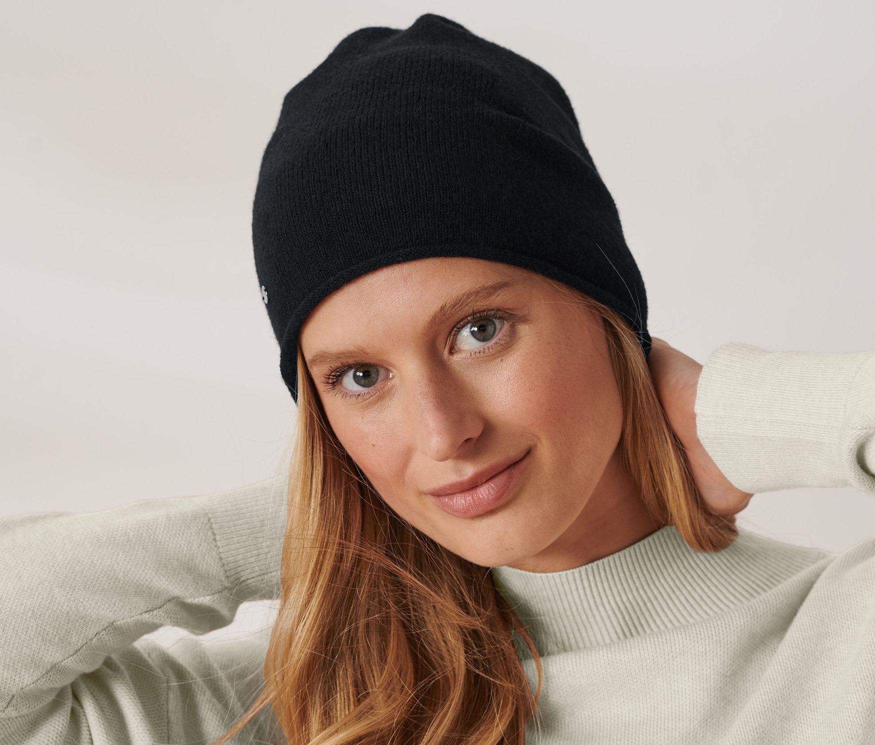 Frau mit braunen Haaren posiert mit Feinstrick-Beanie, schwarz.