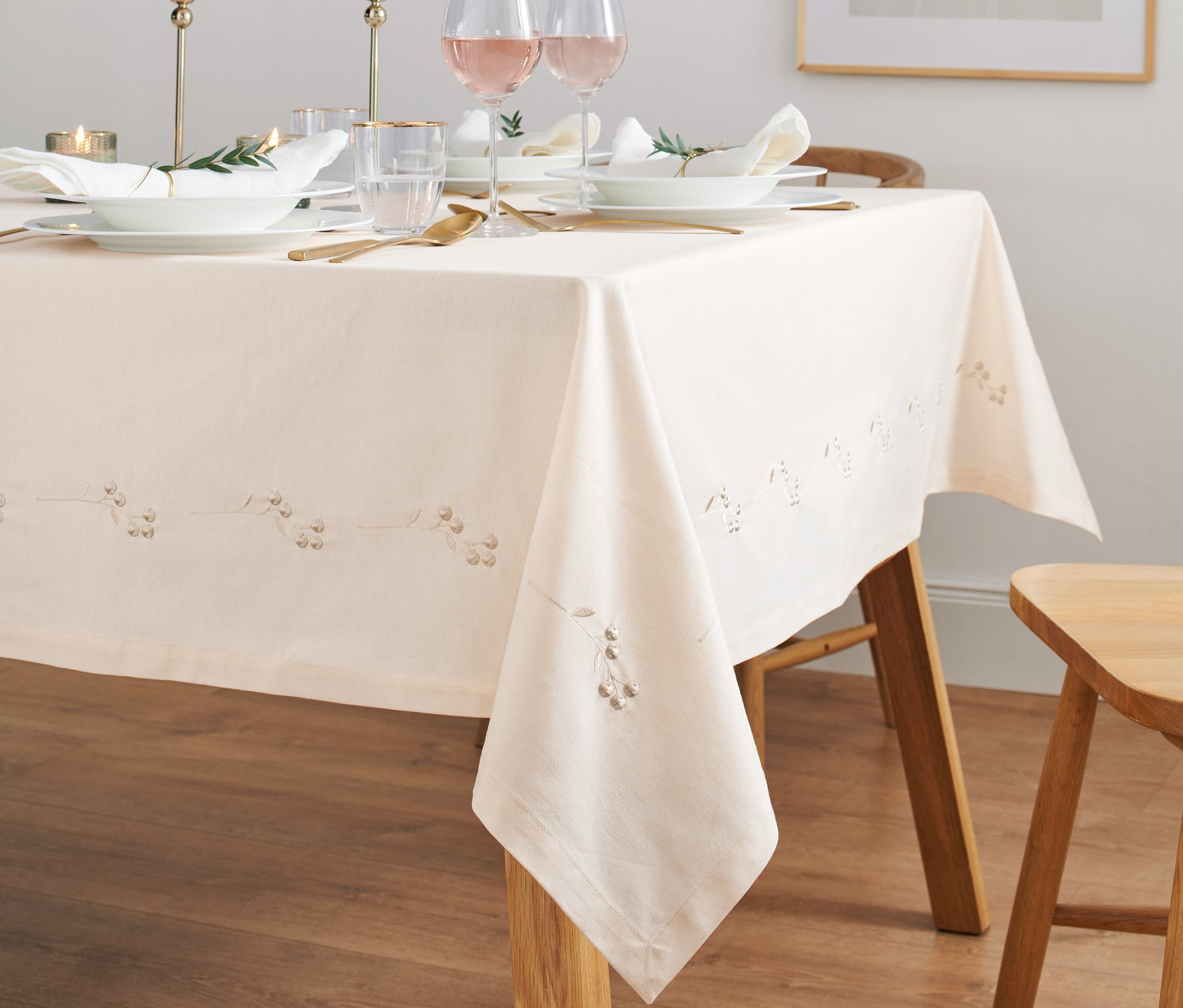 Ein gedeckter Tisch mit einer bestickten Tischdecke, Tellern, Gläsern und Kerzen.