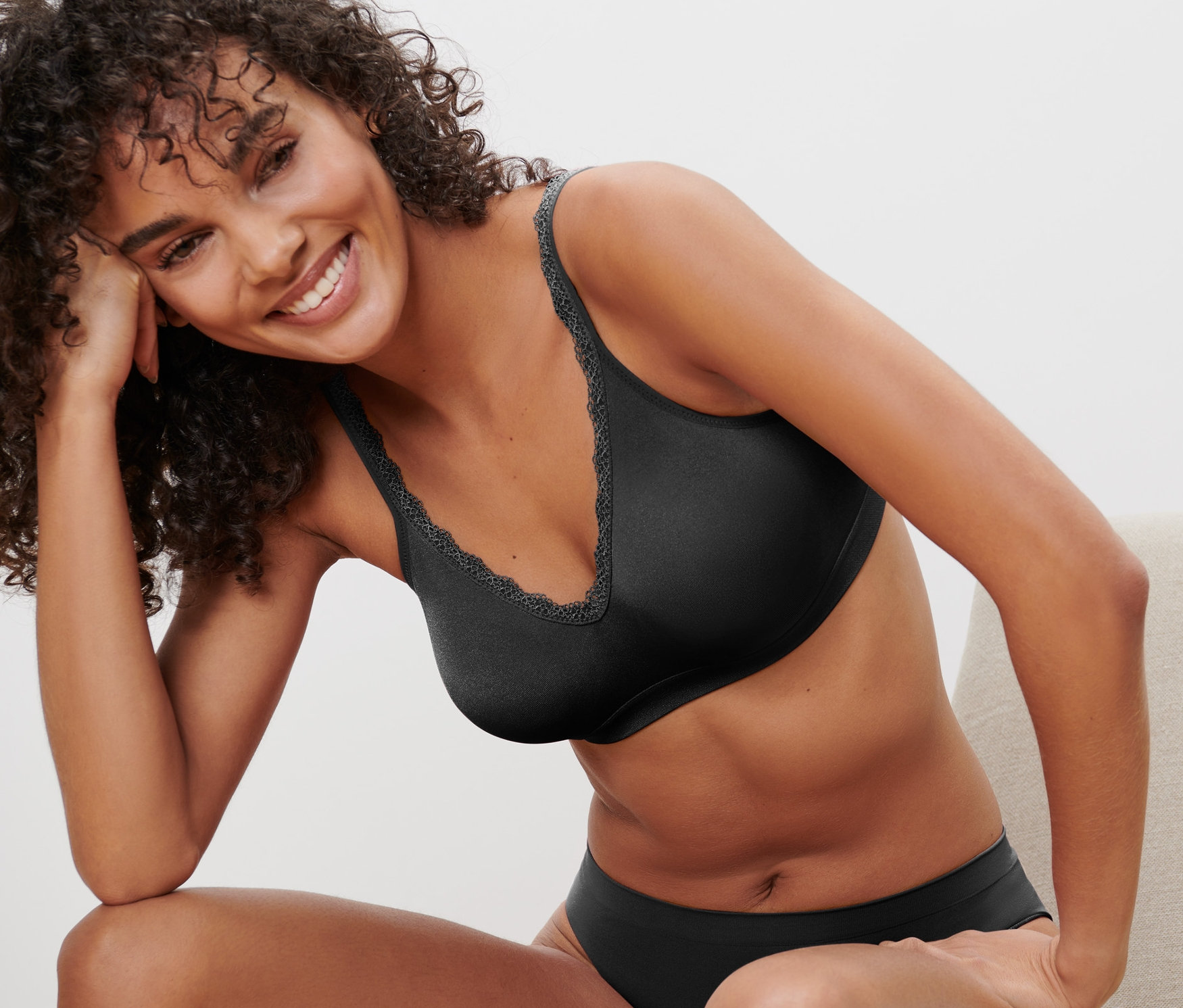Lächelnde Frau sitzt auf einem Stuhl und trägt einen schwarzen Seamless-Soft-BH.