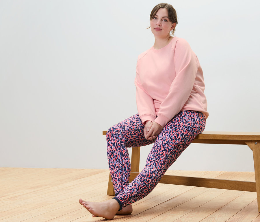 Frau sitzt auf einer Bank in einem roséfarbenen Yoga-Sweatshirt und einer Wende-Sporttight in Rosa/Navy.