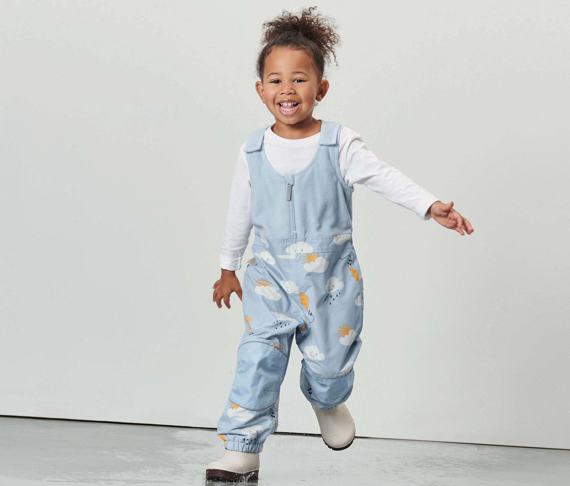 Lächelndes kleines Mädchen in einer Kleinkind Thermo-Regenhose mit Wolkenmuster.