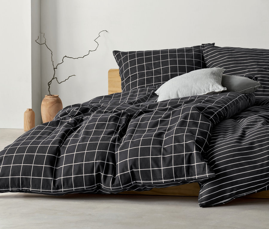 Anthrazitfarbene Biber-Bettwäsche mit Karomuster und Streifenmuster auf einem Bett.