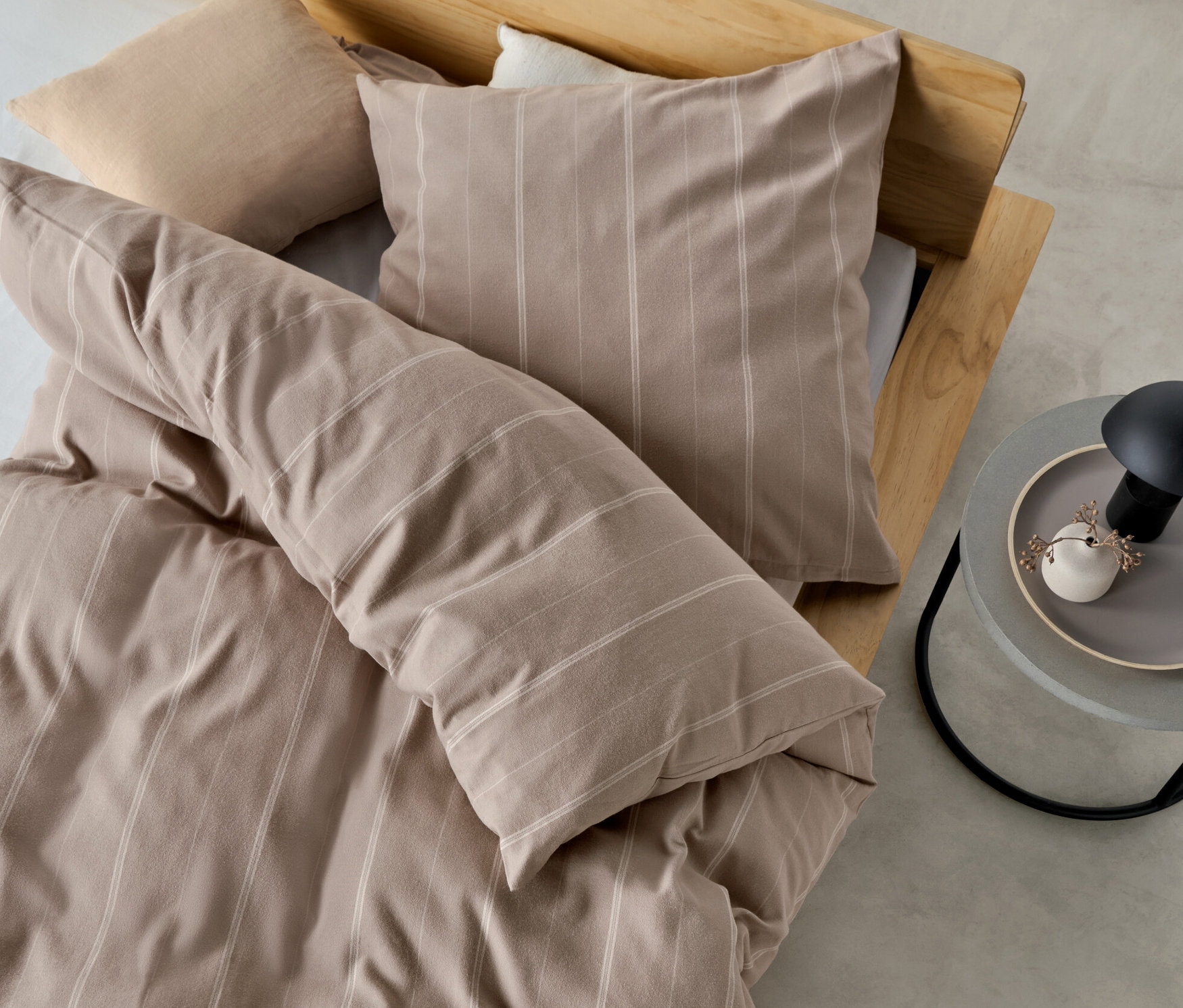 Draufsicht auf ein Bett mit taupefarbener Flanell-Bettwäsche in Normalgröße mit Streifen.
