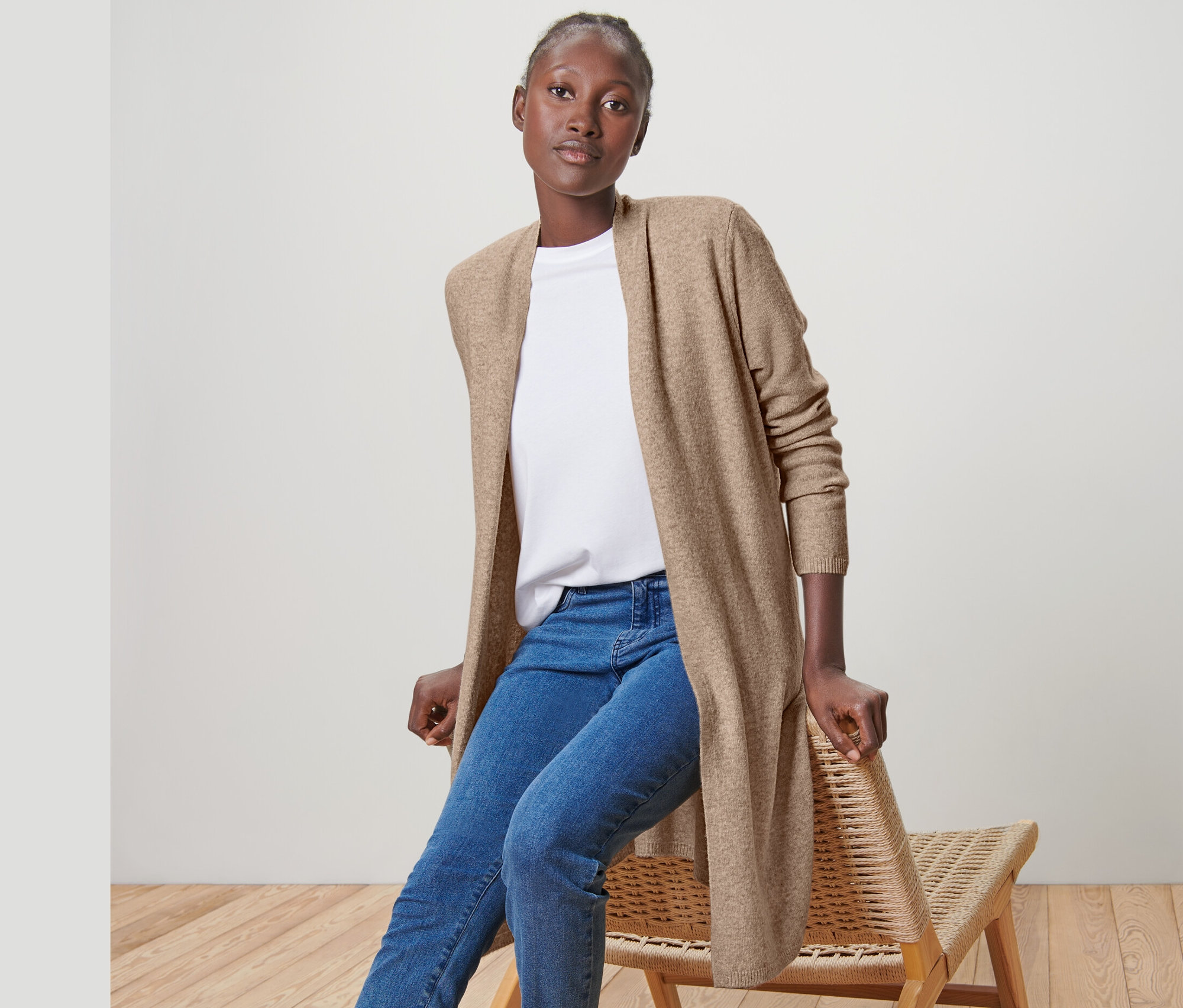 Frau sitzt auf einem Stuhl und trägt einen offenen Longcardigan, Jeans und Turnschuhe.