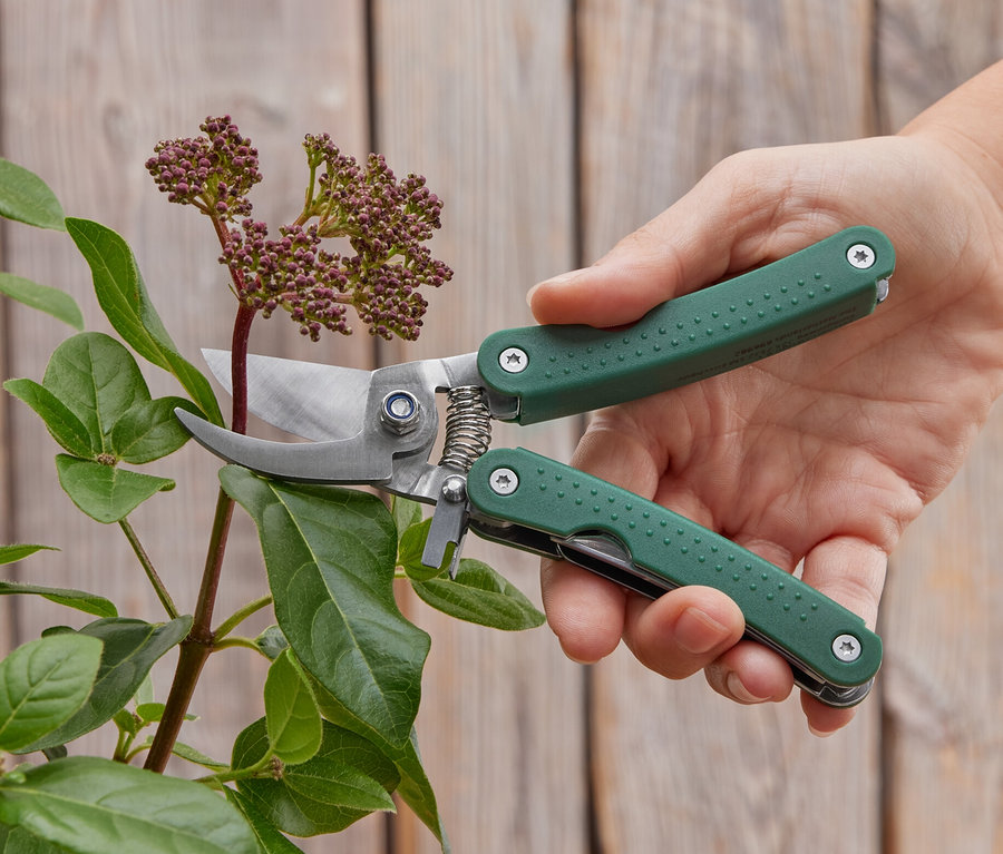 Eine Hand schneidet eine Pflanze mit einer Multifunktions-Gartenschere.